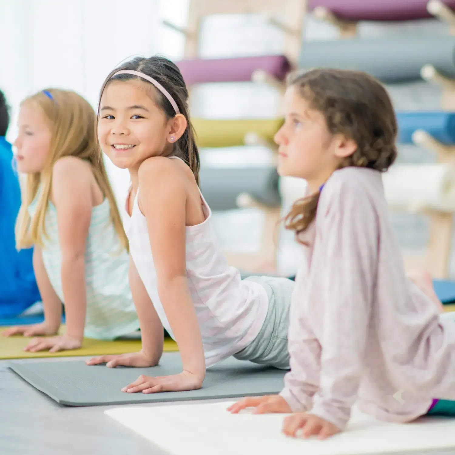 Grupo de niñas practicando yoga en una postura de extensión, en un ambiente luminoso y relajado; aparece una etiqueta con la palabra Todos los niveles.